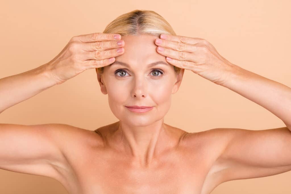 Older woman touching her face after receiving skin tightening treatment for younger, smoother skin