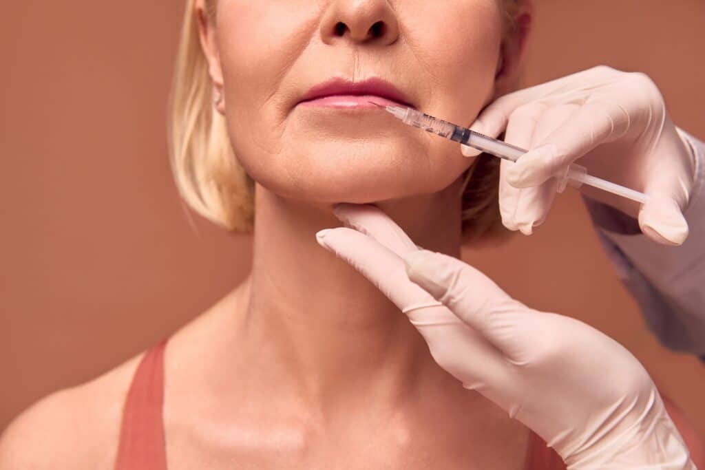Close up of an older woman having dermal fillers injected into her lips for a fuller look