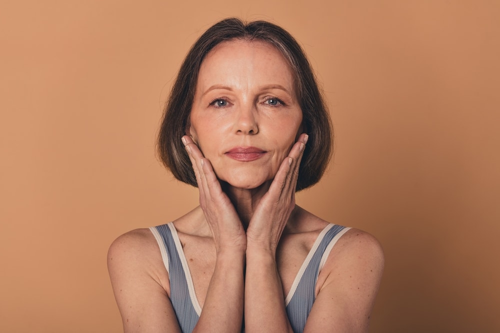 Older woman touching her face in need of microneedling for fine lines and wrinkles.