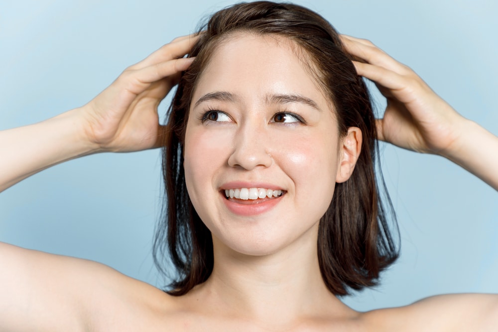 Close up of a beautiful young woman looking away from the camera while happily touching her full, thick hair.