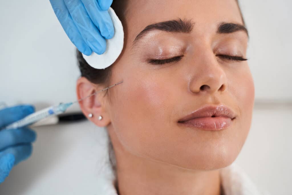 Close-up of a calm, happy woman receiving dermal filler injections to her cheeks for a brighter look