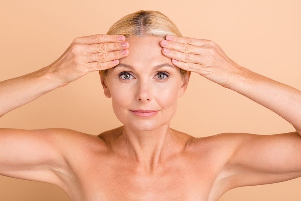 Older woman pulling on her forehead to show how she needs non-surgical skin tightening treatment.