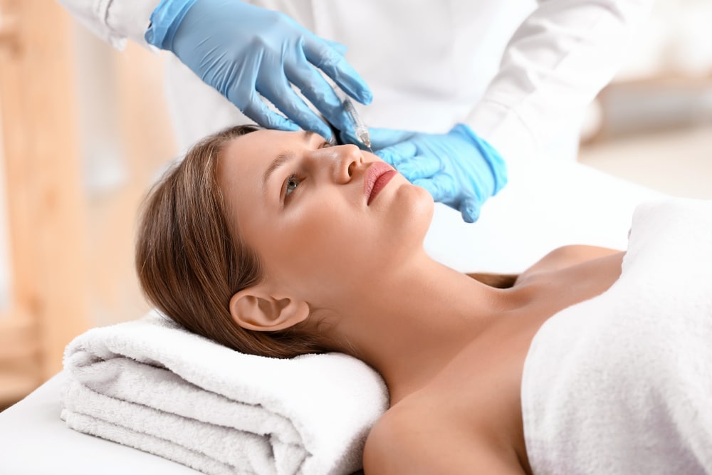 Woman laying down and receiving Dysport injections to her face in a spa-like setting. Woman laying down and receiving Dysport injections to her face in a spa-like setting.